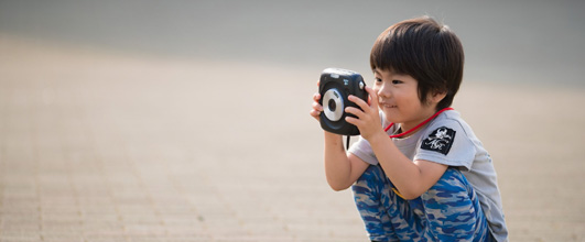 写真素材サイト「PAKUTASO」より、「インスタントカメラに興味津々の子供」。ぜんせーさんの作品。 アイキャッチ画像。
