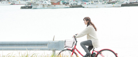 素材サイト「PAKUTASO」より、「自転車で買い物に出かける女性」。g.O.R.i さんの作品。モデルは河村友歌さん。千葉県いすみ市の観光PR写真素材。 アイキャッチ画像。