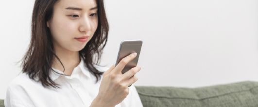 素材サイト「写真AC」より、ソファに座ってスマートフォンを操作する女性 。TicTacさんの作品。 アイキャッチ画像。