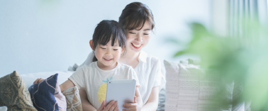 素材サイト「写真AC」より、 ソファに座ってオンラインコミュニケーションをする親子 。coji_coji_acさんの作品。 アイキャッチ画像。